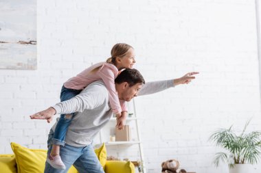 Baba evde heyecanlı bir kızı sırtında taşırken sineklerle hareket ediyor.
