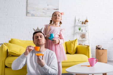 Baba ve kız ellerinde oyuncak bardaklarla evde prensçilik oynuyorlar.