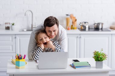 Heyecanlı baba-kız online ders sırasında dizüstü bilgisayara bakıyor.