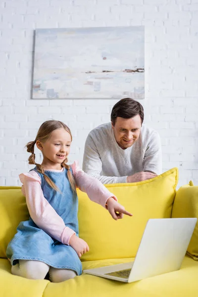 Glimlachende Vader Buurt Dochter Wijzen Naar Laptop Tijdens Het Kijken — Stockfoto