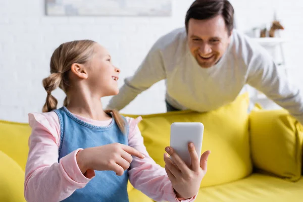 Leende Flicka Pekar Mobiltelefon Nära Far Skrattar Suddig Bakgrund — Stockfoto