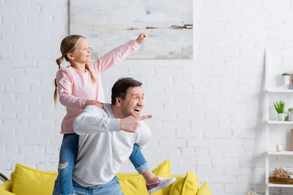 Animado Homem Apontando Com Dedo Enquanto Piggybacking Filha Mostrando Vitória — Fotografia de Stock