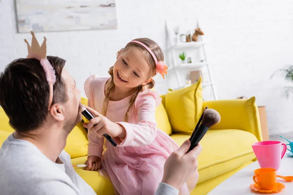 Man Toy Crown Holding Cosmetic Brushes While Cheerful Daughter Applying — Stock Photo, Image
