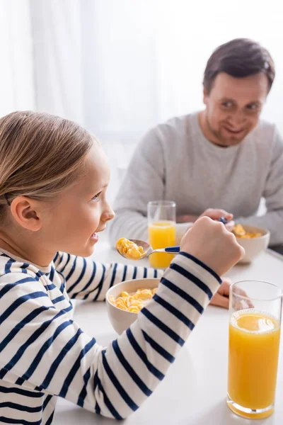 Meisje Eten Cornflakes Buurt Glimlachende Vader Wazig Achtergrond — Stockfoto