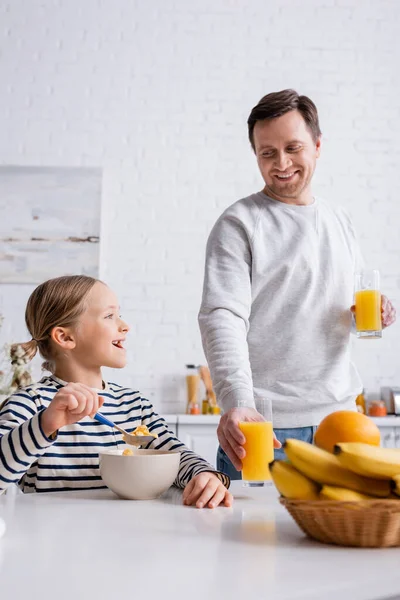 Homem Sorrindo Segurando Suco Laranja Perto Filha Comendo Flocos Milho — Fotografia de Stock