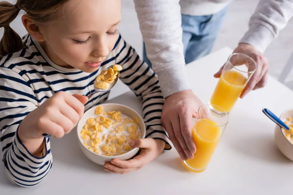 Chica Comiendo Copos Maíz Cerca Padre Vasos Jugo Naranja —  Fotos de Stock