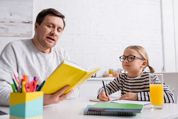 Padre Leyendo Libro Hija Sosteniendo Pluma Cerca Del Cuaderno — Foto de Stock