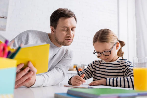 Pai Segurando Livro Perto Filha Escrevendo Caderno Fazer Lição Casa — Fotografia de Stock