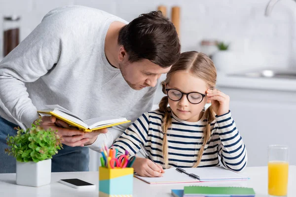 Father Holding Book Daughter Writing Notebook Blurred Foreground — Stock Photo, Image