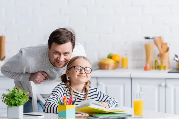 Feliz Padre Mirando Cámara Cerca Sonreír Chica Haciendo Tarea Cocina — Foto de Stock