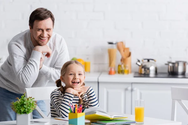 Alegre Padre Hija Sonriendo Cámara Cerca Mesa Con Cuadernos Cocina — Foto de Stock