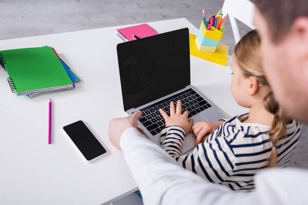 high angle view of girl typing on laptop near father on blurred foreground