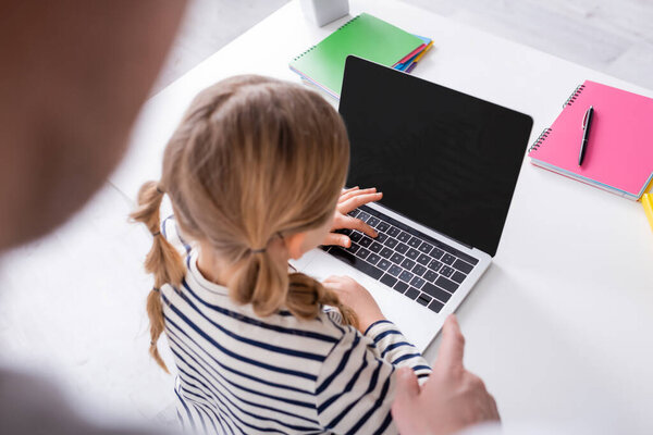 high angle view of girl near laptop and father pointing with finger on blurred foreground
