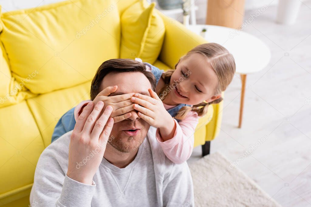 cheerful girl covering eyes of father while playing guess who game