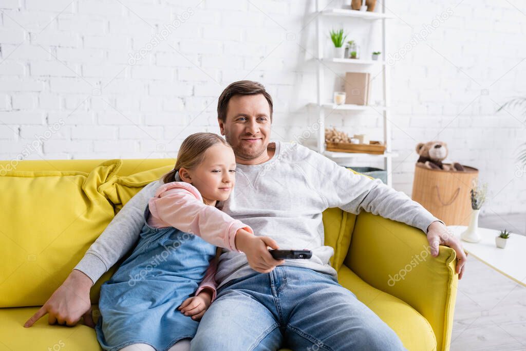 smiling man watching tv with daughter clicking channels on remote controller