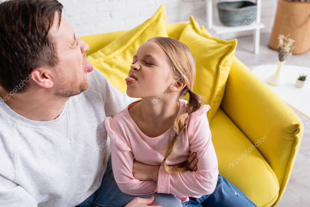 father and daughter sticking out tongues to each other at home