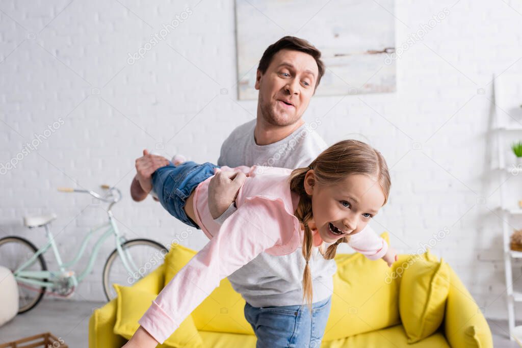 father holding cheerful daughter while having fun at home