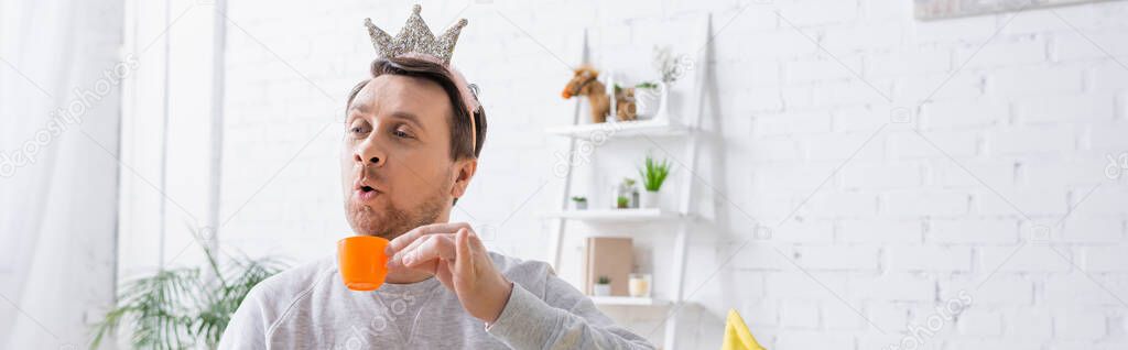 adult man playing king and holding toy cup at home, banner