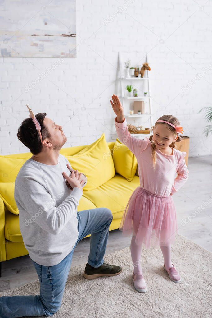 father in toy crown standing on knee and inviting daughter to dance