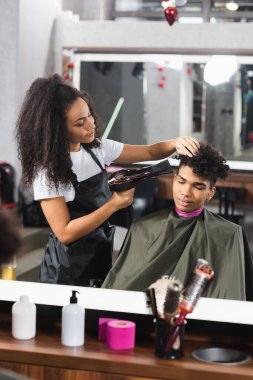 Müşteriyle çalışırken saç kurutma makinesi kullanan Afrikalı Amerikalı kuaför. 