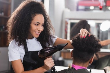 Pozitif Afro-Amerikan kuaför müşterinin yanında saç kurutma makinesi tutuyor. 