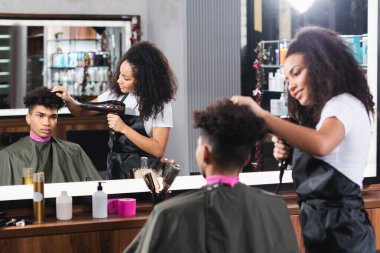 Afrikalı Amerikalı kuaför kuaförde genç bir adamın saçını kurutuyor. 