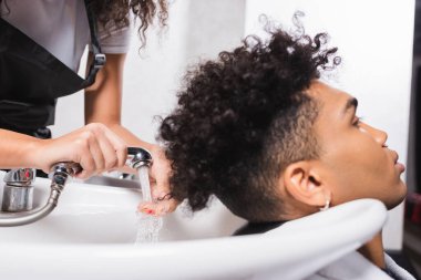 Afro-Amerikan kuaförün ve kuafördeki genç müşterinin ellerinde duş. 