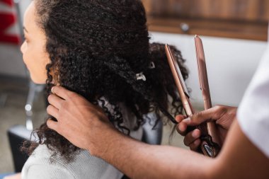 Afrikalı Amerikalı kuaför müşterinin yanında saç düzleştirici tutuyor. 