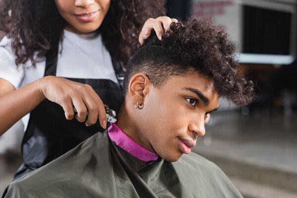 African american client sitting near hairdresser with trimmer on blurred background 