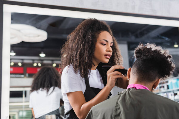 Young african american hairdresser trimming hair of curly client 