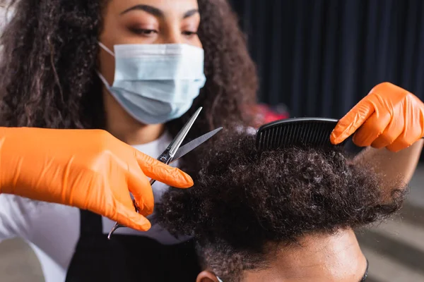 隔離中にサロンで顧客と働くアフリカ系アメリカ人の美容師の手にはさみと櫛 — ストック写真