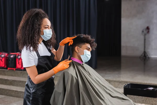 医療用マスクとラテックス手袋のアフリカ系アメリカ人美容師保持はさみとクライアントの組み合わせ髪 — ストック写真