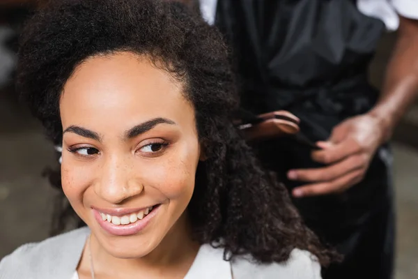 Fröhliche Afrikanisch Amerikanische Frau Sitzt Neben Friseur Mit Haarbügeleisen Auf — Stockfoto