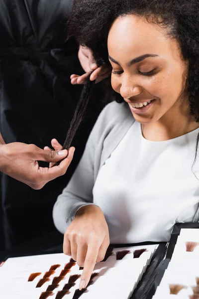 ヘアスタイリストの近くのヘアカラーサンプルを指す陽気なアフリカ系アメリカ人のクライアント — ストック写真