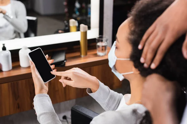 Client Afro American Mască Medicală Arătând Spre Smartphone Lângă Coafor — Fotografie, imagine de stoc