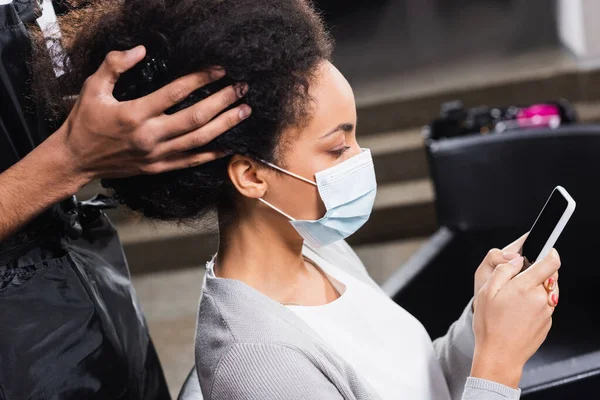Αφροαμερικανός Πελάτης Ιατρική Μάσκα Χρησιμοποιώντας Smartphone Κοντά Κομμωτή Ποδιά — Φωτογραφία Αρχείου