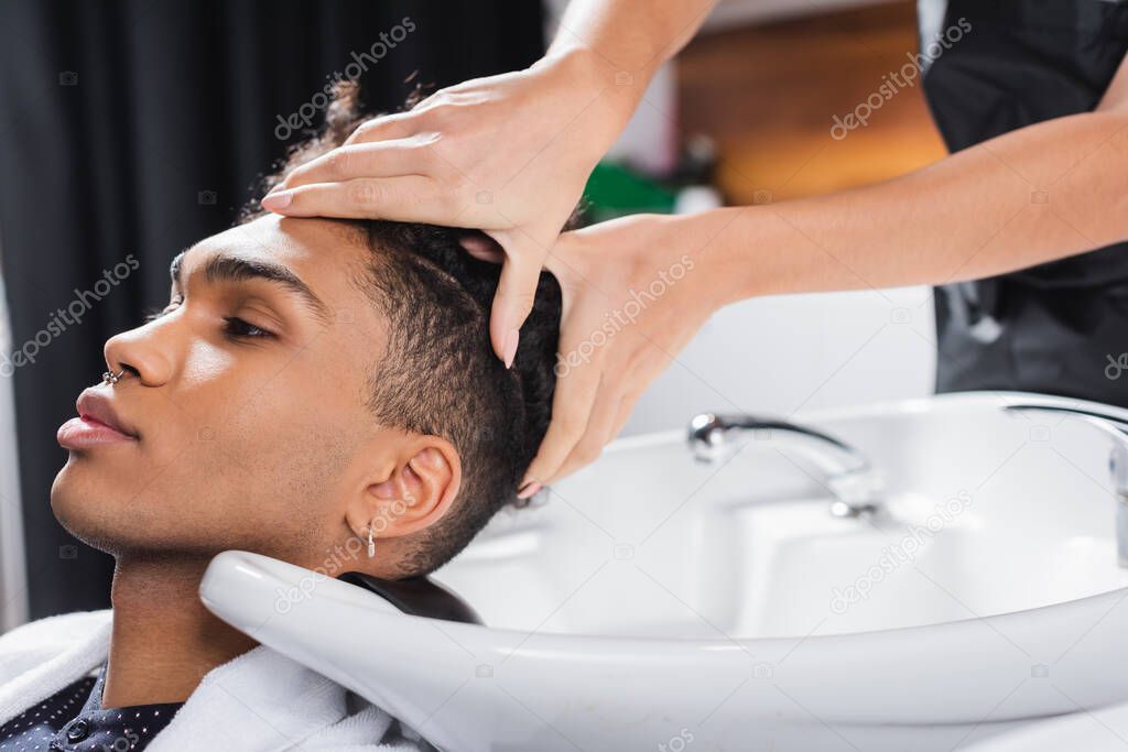 Hairstylist washing head of african american client near sink in salon 