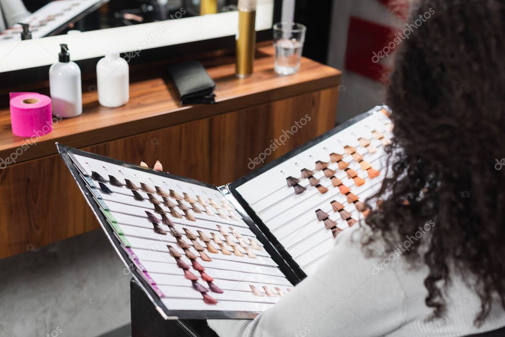 African american woman on blurred foreground holding hair color swatches in salon 