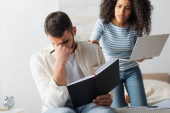 man holding notebook and covering face near worried african american girlfriend on blurred background 