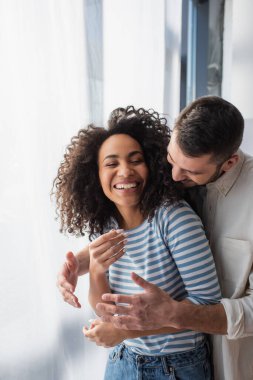 Mutlu çok ırklı çift evde sarılırken gülümsüyor.