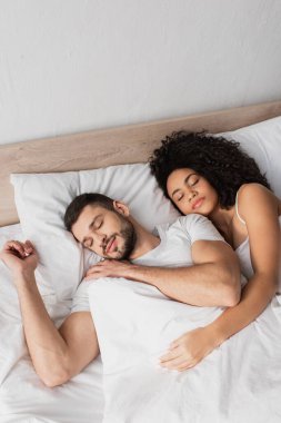 Yatakta uyuyan çok ırklı çiftin yüksek açılı görüntüsü 