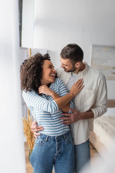 Alegre Pareja Multiétnica Riendo Mientras Abraza Casa —  Fotos de Stock