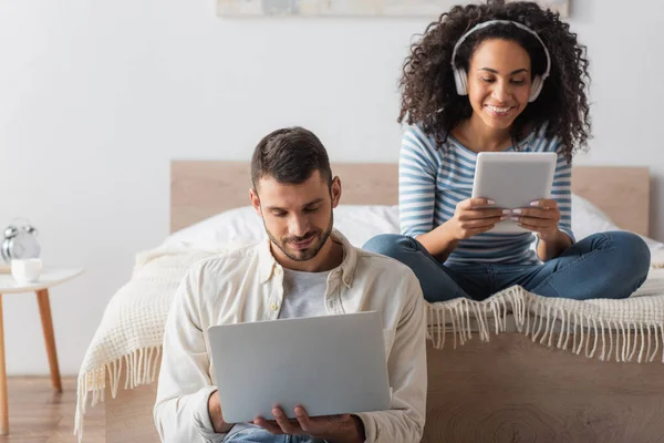 アフリカ系アメリカ人の女性が音楽を聴きながらノートパソコンでボーイフレンドの近くのデジタルタブレットを使って — ストック写真