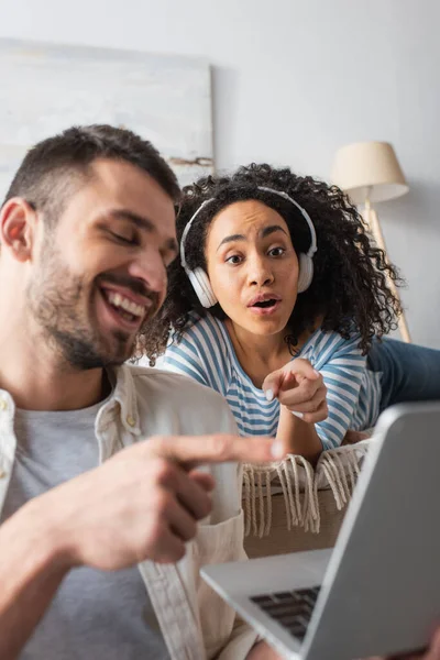 Feliz Pareja Interracial Riendo Señalando Con Los Dedos Computadora Portátil — Foto de Stock