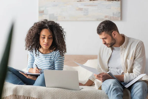 African American Woman Writing Notebook Boyfriend Looking Taxes Papers Laptop — Stock Photo, Image