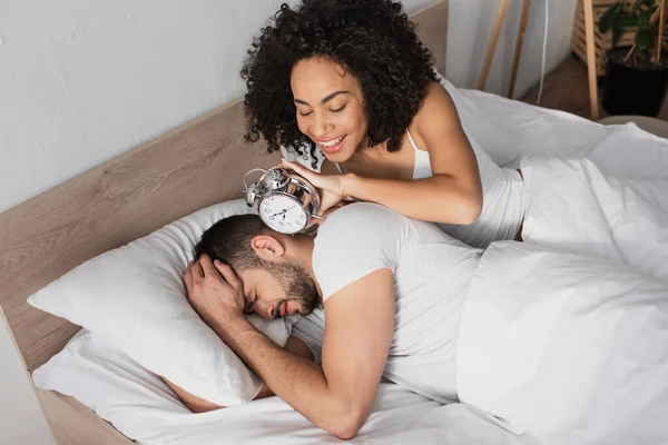 Lycklig Afrikansk Amerikansk Kvinna Håller Väckarklocka Nära Missnöjd Man Sover — Stockfoto
