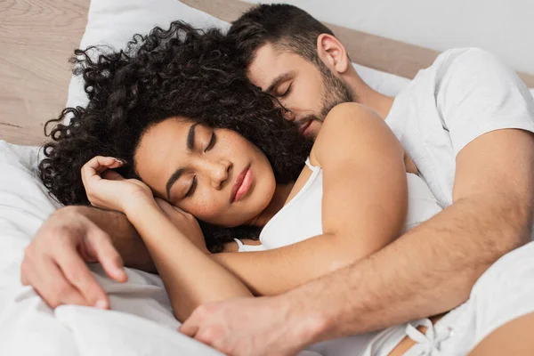 multiethnic man and woman hugging while sleeping in bed