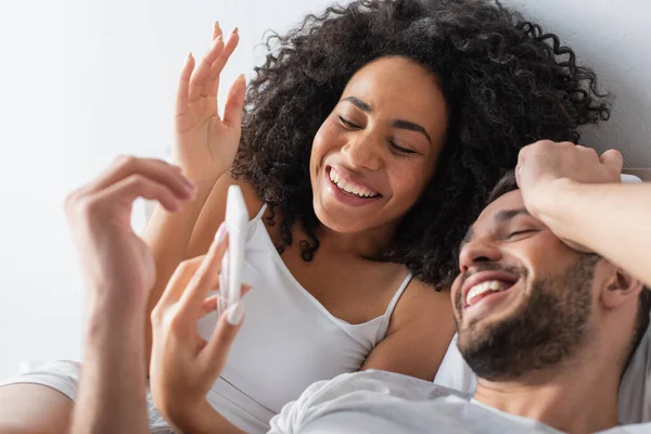 Alegre Casal Multiétnico Sorrindo Enquanto Olha Para Telefone Móvel — Fotografia de Stock