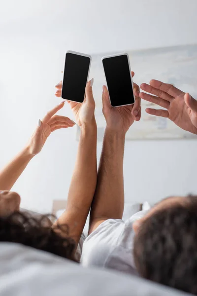 Pareja Multiétnica Borrosa Utilizando Teléfonos Inteligentes Con Pantalla Blanco Dormitorio — Foto de Stock
