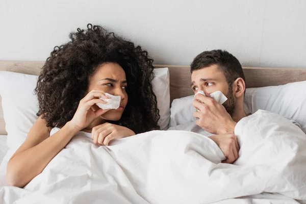 Sick Interracial Couple Holding Napkins Sneezing While Looking Each Other — Stock Photo, Image